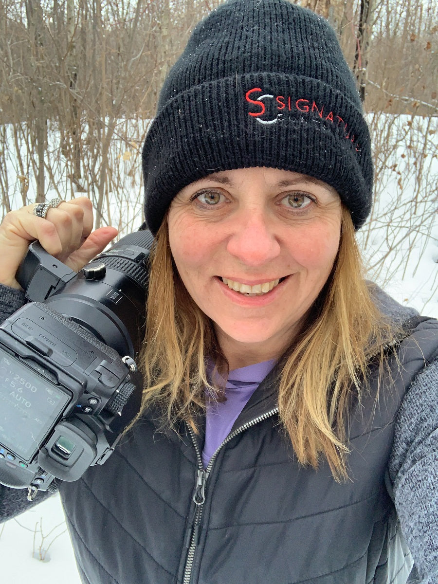 Photo of Donna Feledichuk Wildlife Photographer in the field. She is holding her camera and is dressed for the winter conditions. 